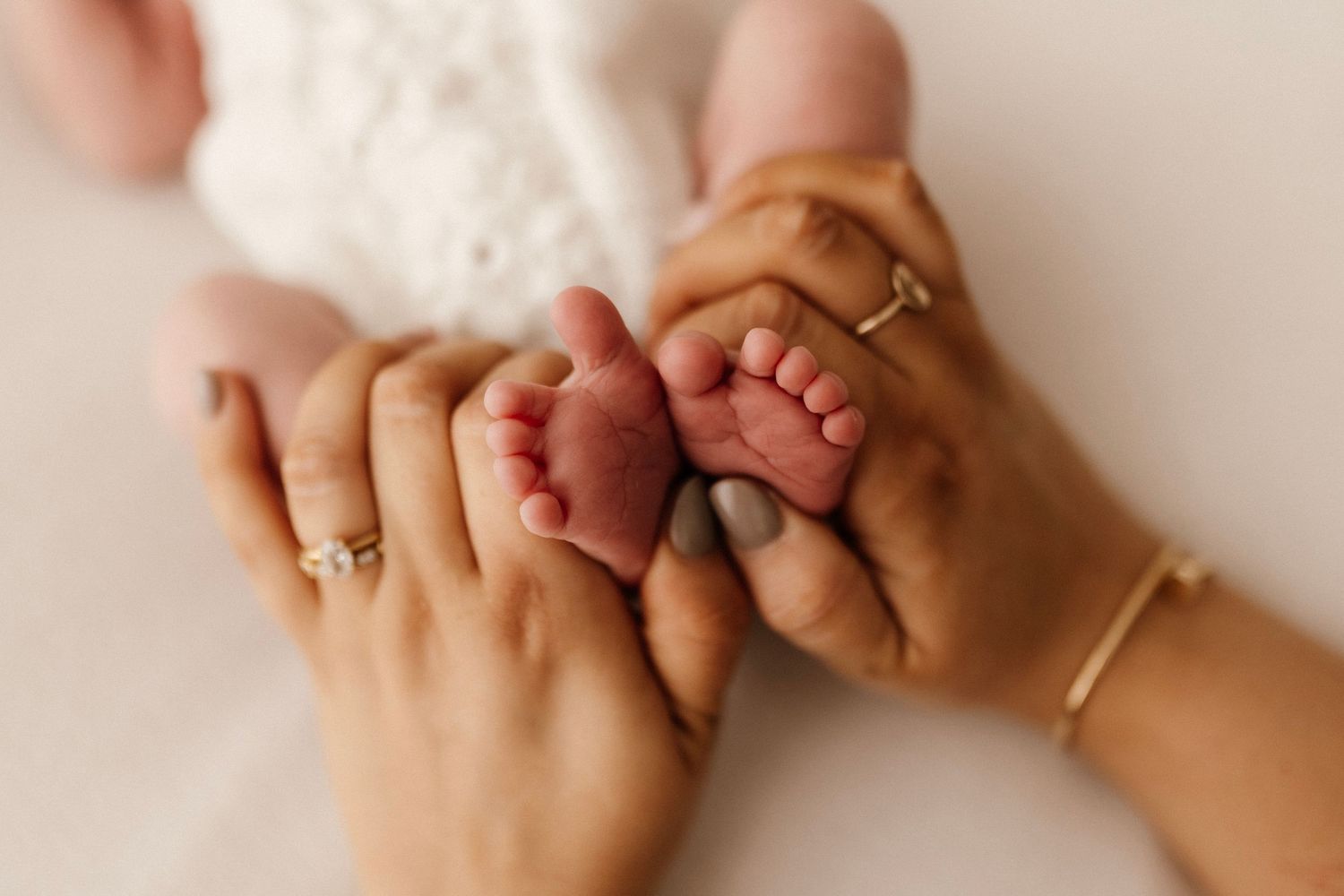 Close up of tiny baby feet being held by adult hands wearing gold rings.