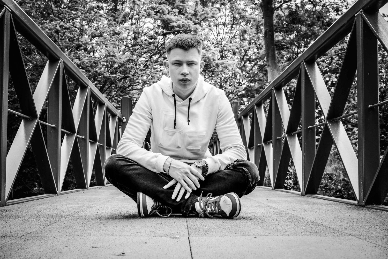 Black and white portrait of a person sitting cross-legged on a bridge.