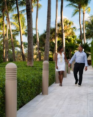 Couple holding hands walking along a palm tree-lined pathway at a tropical resort.