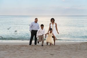 Happy family of four walking together on a sandy beach at sunset.