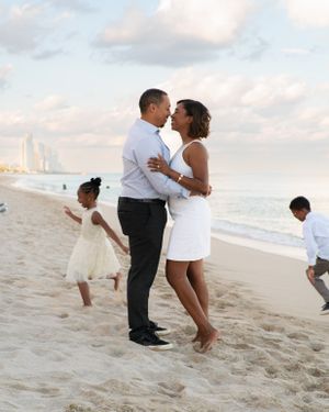 Romantic couple sharing a kiss on the beach while children play around them.