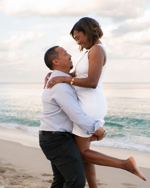 Man lifting woman in his arms on a sandy beach with ocean waves behind them.
