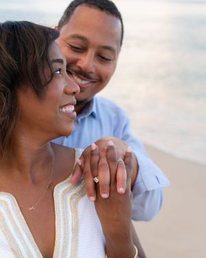Smiling couple holding hands close-up on the beach, woman displaying engagement ring.