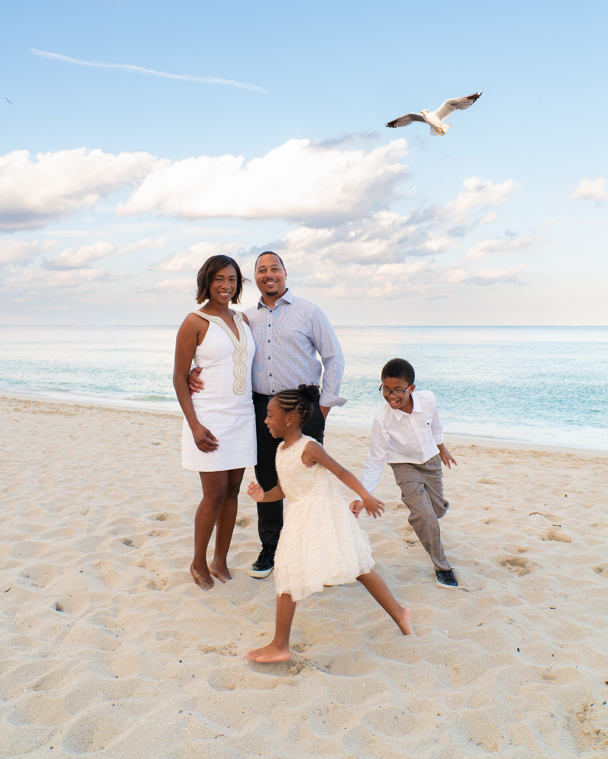 Family of four enjoying a fun moment on the beach as a seagull flies overhead.