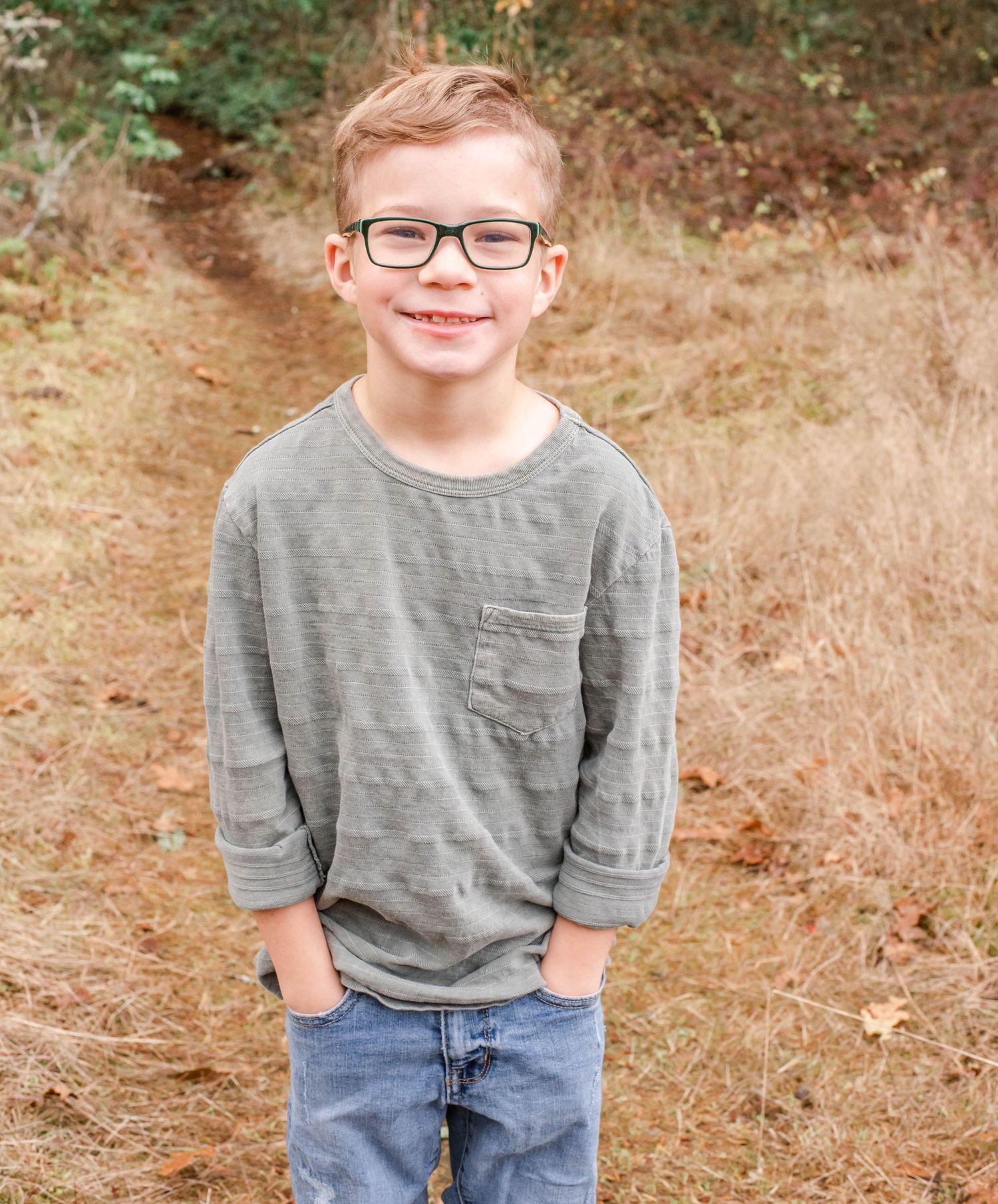 Portrait of young person in gray shirt and glasses against natural background.