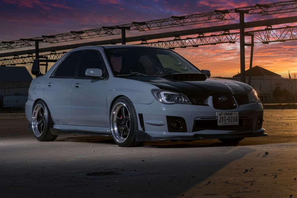 Lowered silver Subaru WRX with custom wheels photographed at sunset against industrial backdrop.