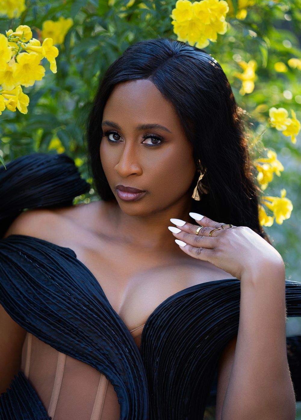 Glamour portrait with black gown against vibrant yellow flowers in natural light.