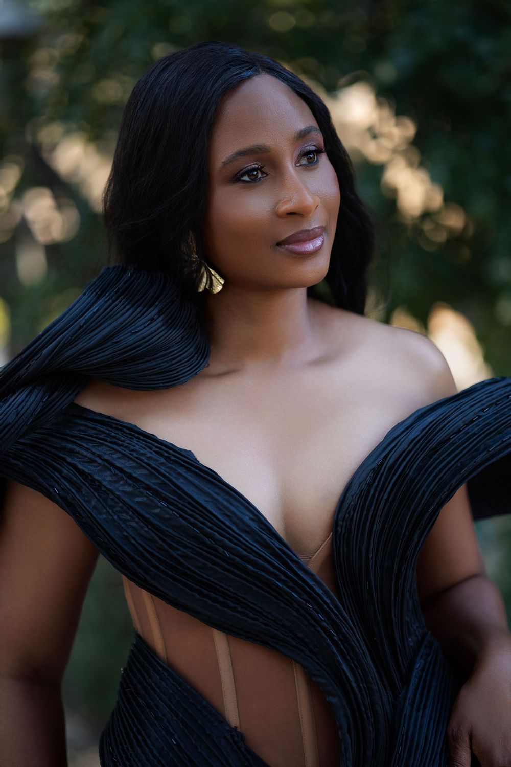 Close-up portrait in structured black evening gown with natural outdoor backdrop.