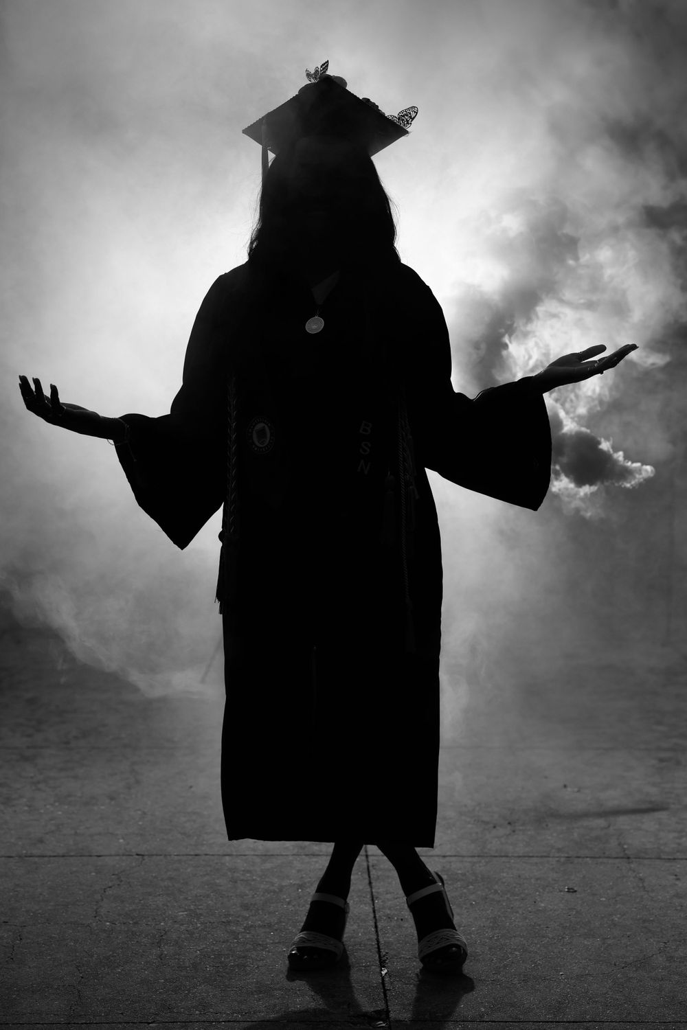 Dramatic silhouette of graduate in cap and gown against cloudy sky.