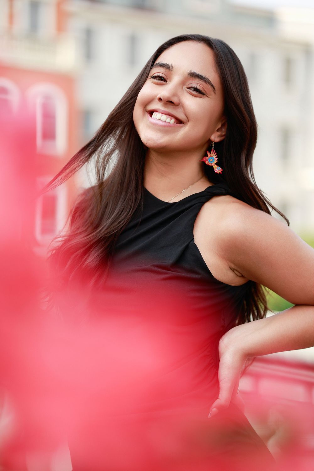 Portrait of someone in black sleeveless top with flowing dark hair and earrings against blurred background.