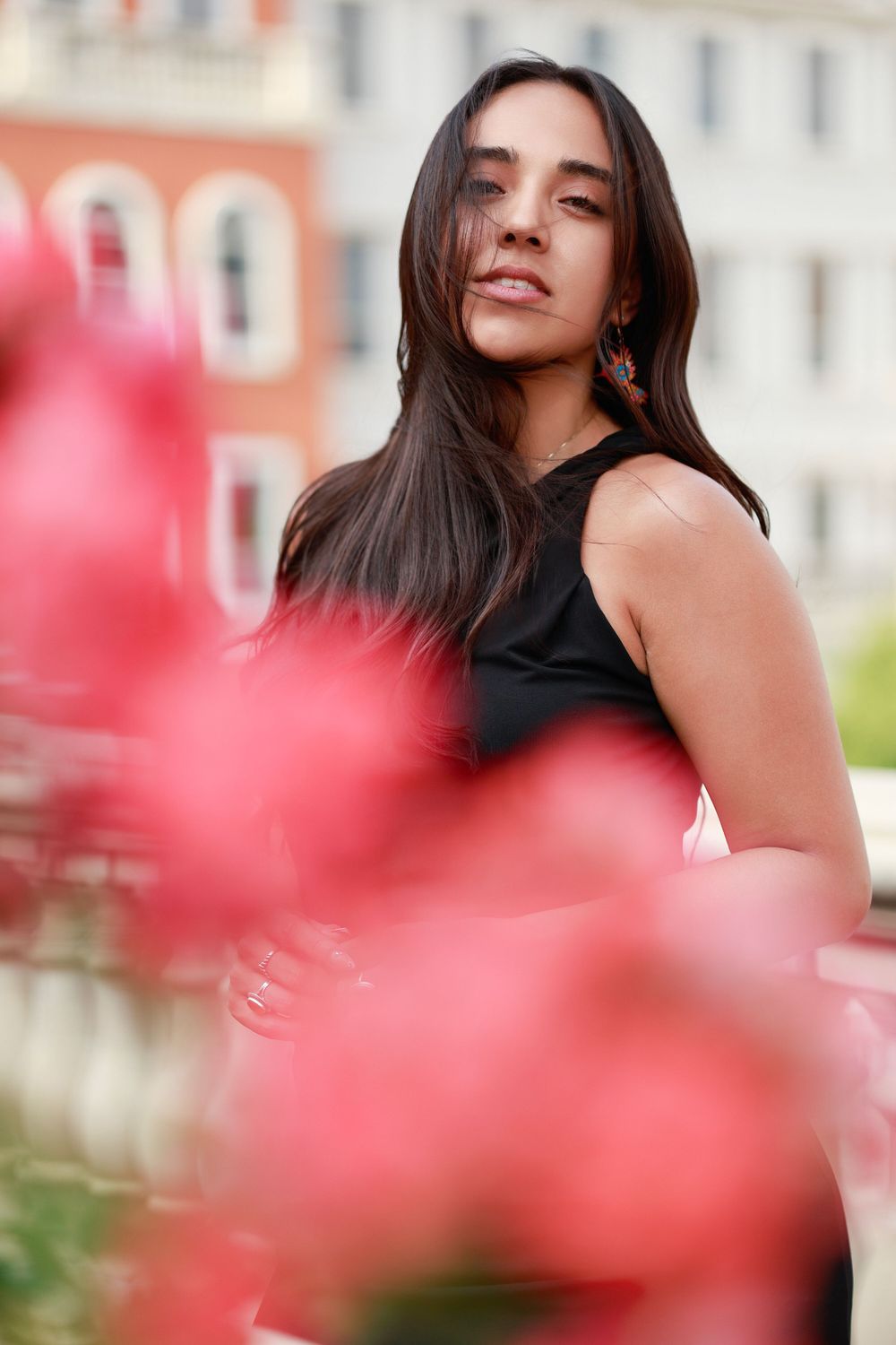 Artistic portrait through red flowers showing person in black top with long dark hair.