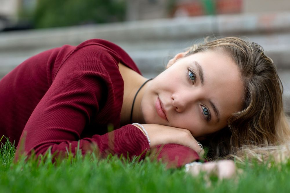 Person in burgundy sweater lying on green grass during outdoor photo session.