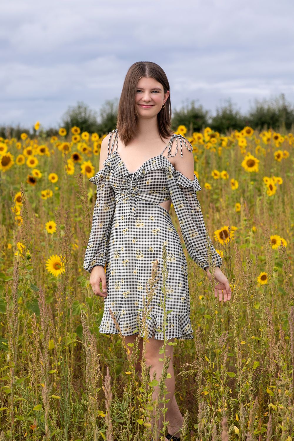 Summer portrait session in sunflower field wearing checkered ruffle dress.
