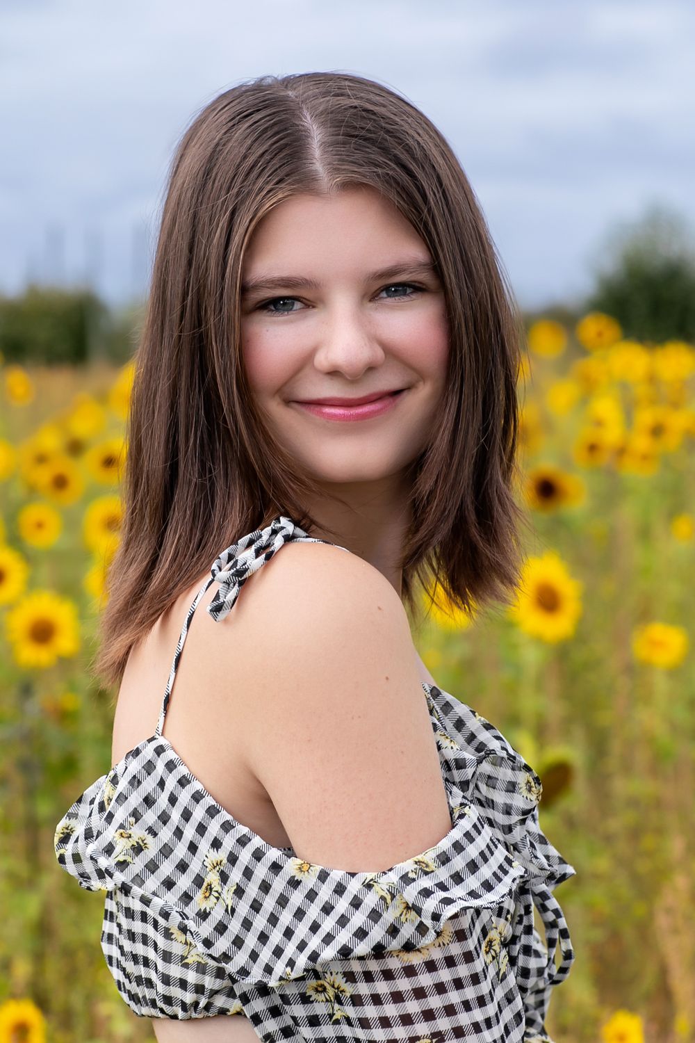 Portrait series in gingham top with sunflower field backdrop.