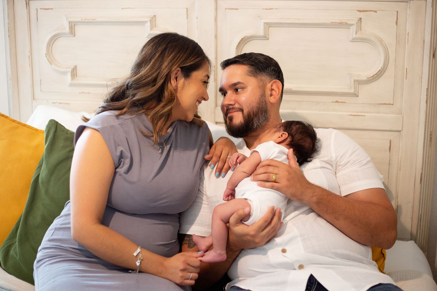 Parents share an intimate moment with their newborn baby on a couch with decorative pillows.