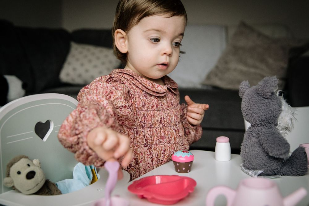 Young child in pink sweater playing with toy tea set and stuffed animals.