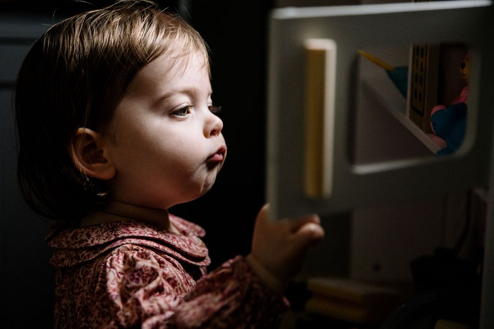 Side profile of child in pink sweater looking at something in dim lighting.