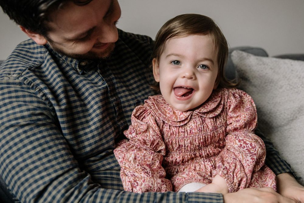 Joyful moment between a child in pink sweater and caregiver on couch.