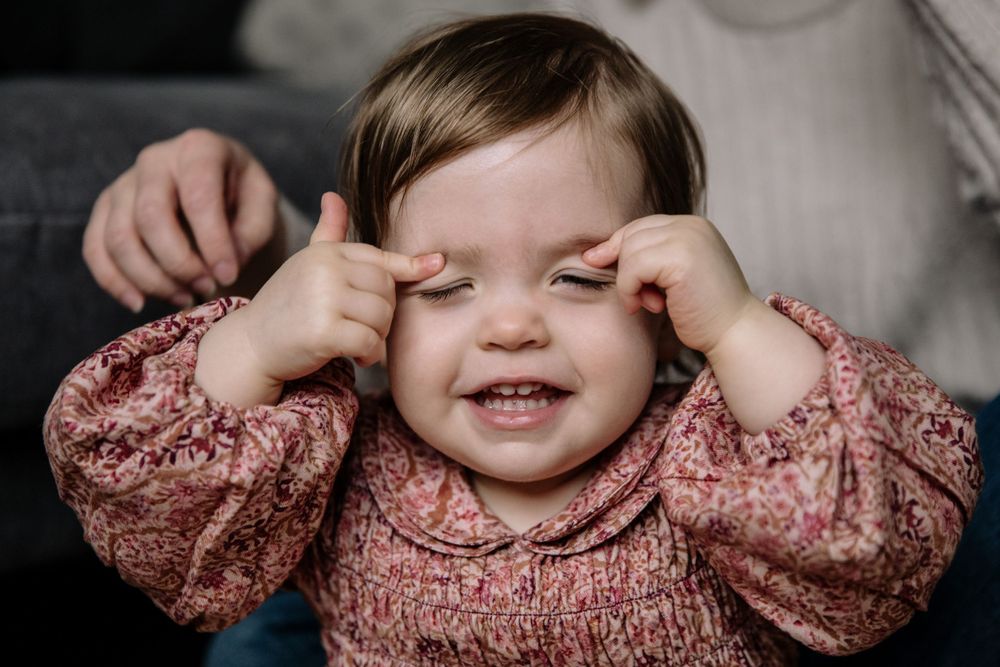 Playfully covering eyes while wearing a pink patterned sweater.