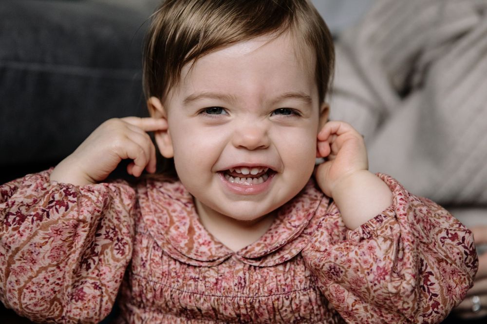 A playful moment captured with hands near ears and a pink floral top.