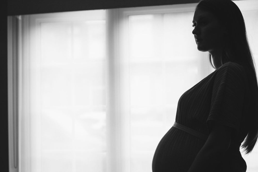 A backlit silhouette shows a pregnant figure against a bright window.