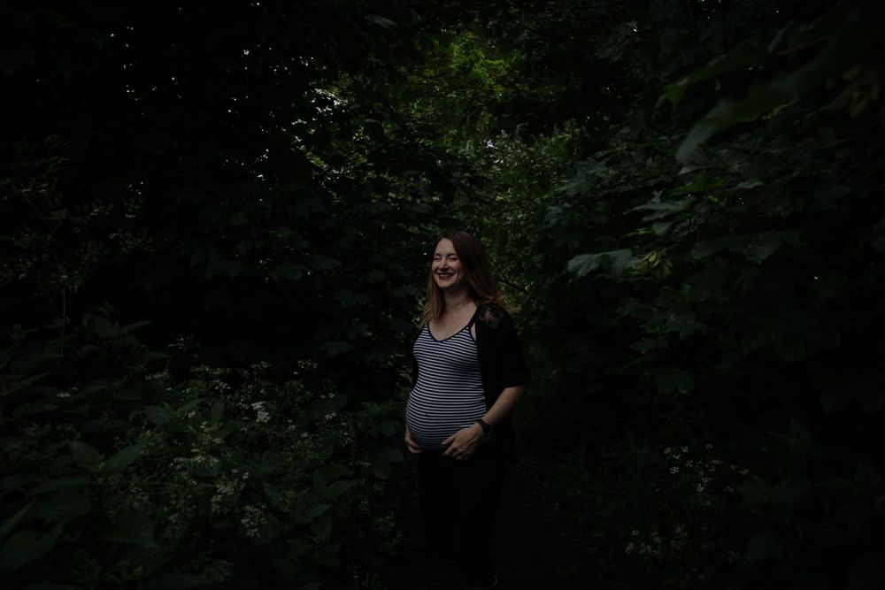 A maternity portrait in a moody forest setting with natural lighting.