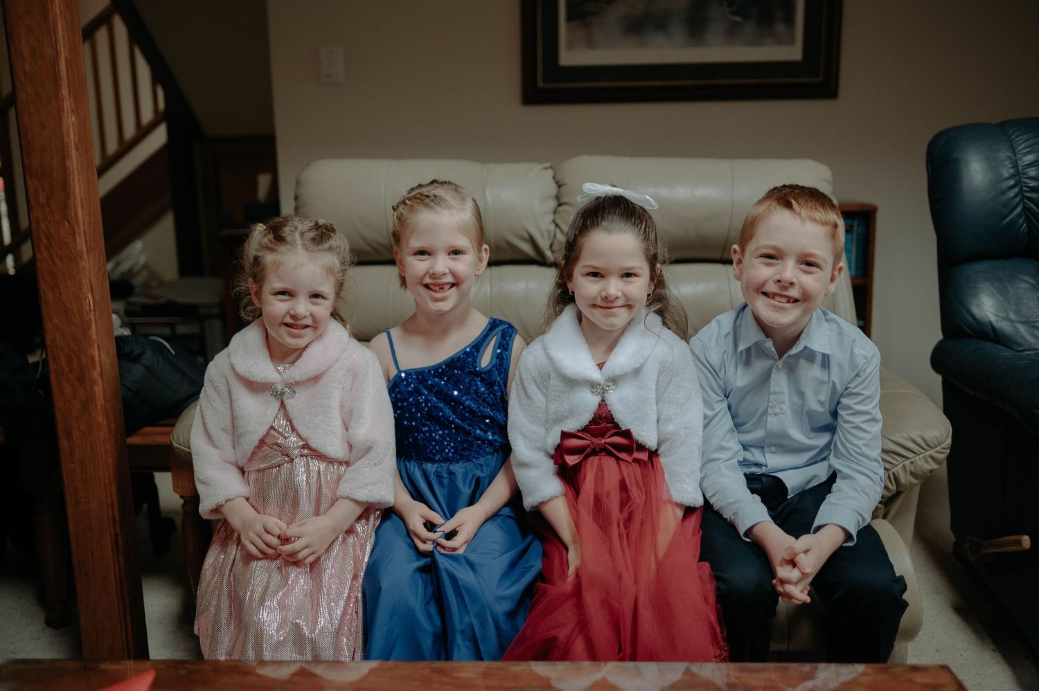 Four children sitting together on a couch dressed in formal attire.
