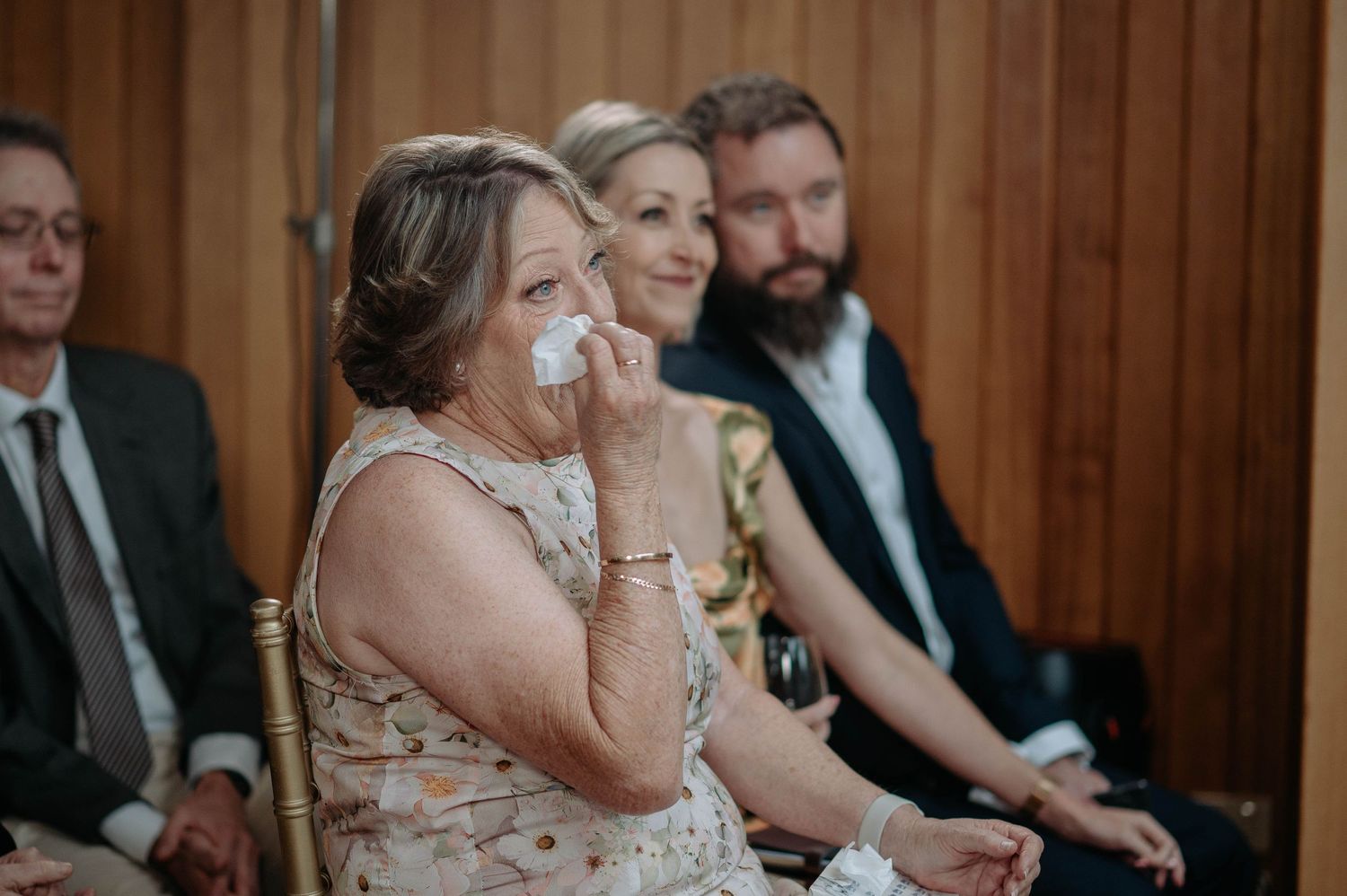 Wedding guests react emotionally during ceremony in wooden venue with warm lighting.