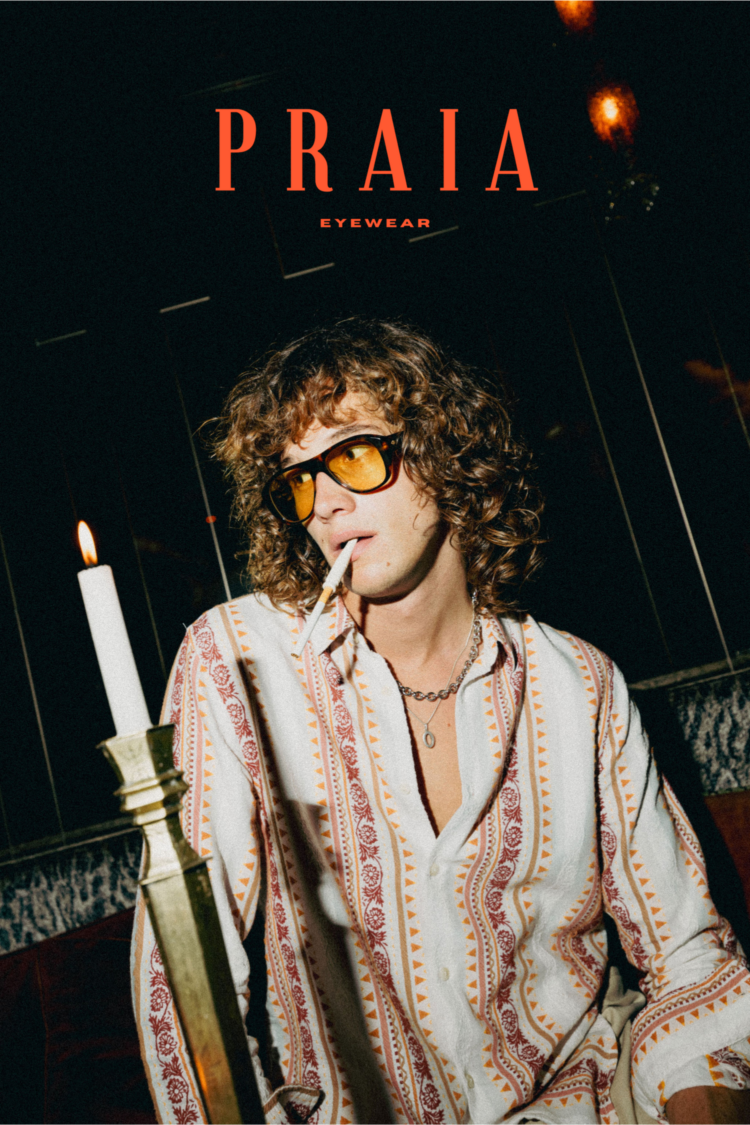 Vintage-styled advertisement for Praia Eyewear featuring model in floral embroidered shirt holding candle in dark moody setting.