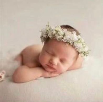 Sleeping newborn wearing white floral crown on neutral backdrop.