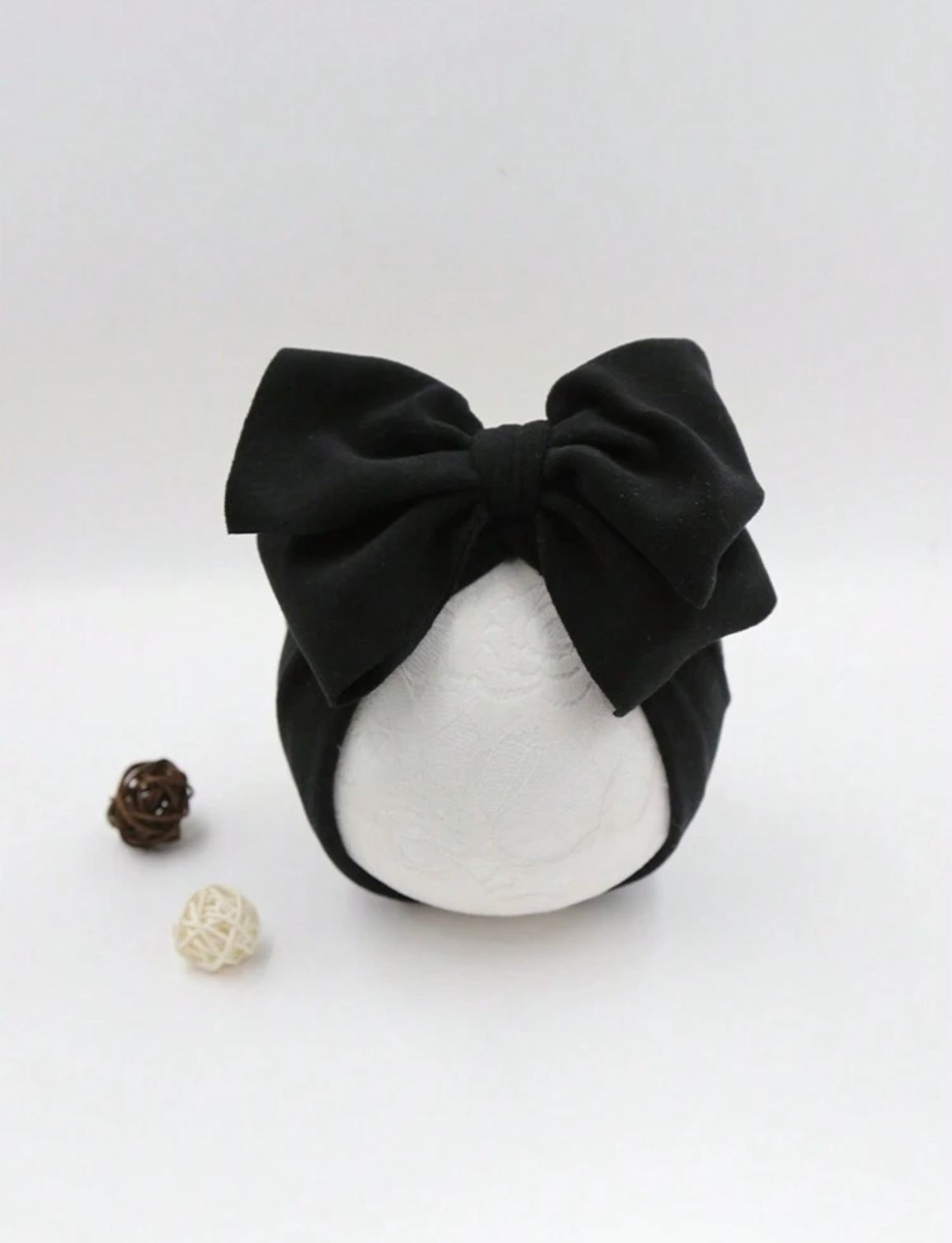 White headband with large black bow photographed against white background.