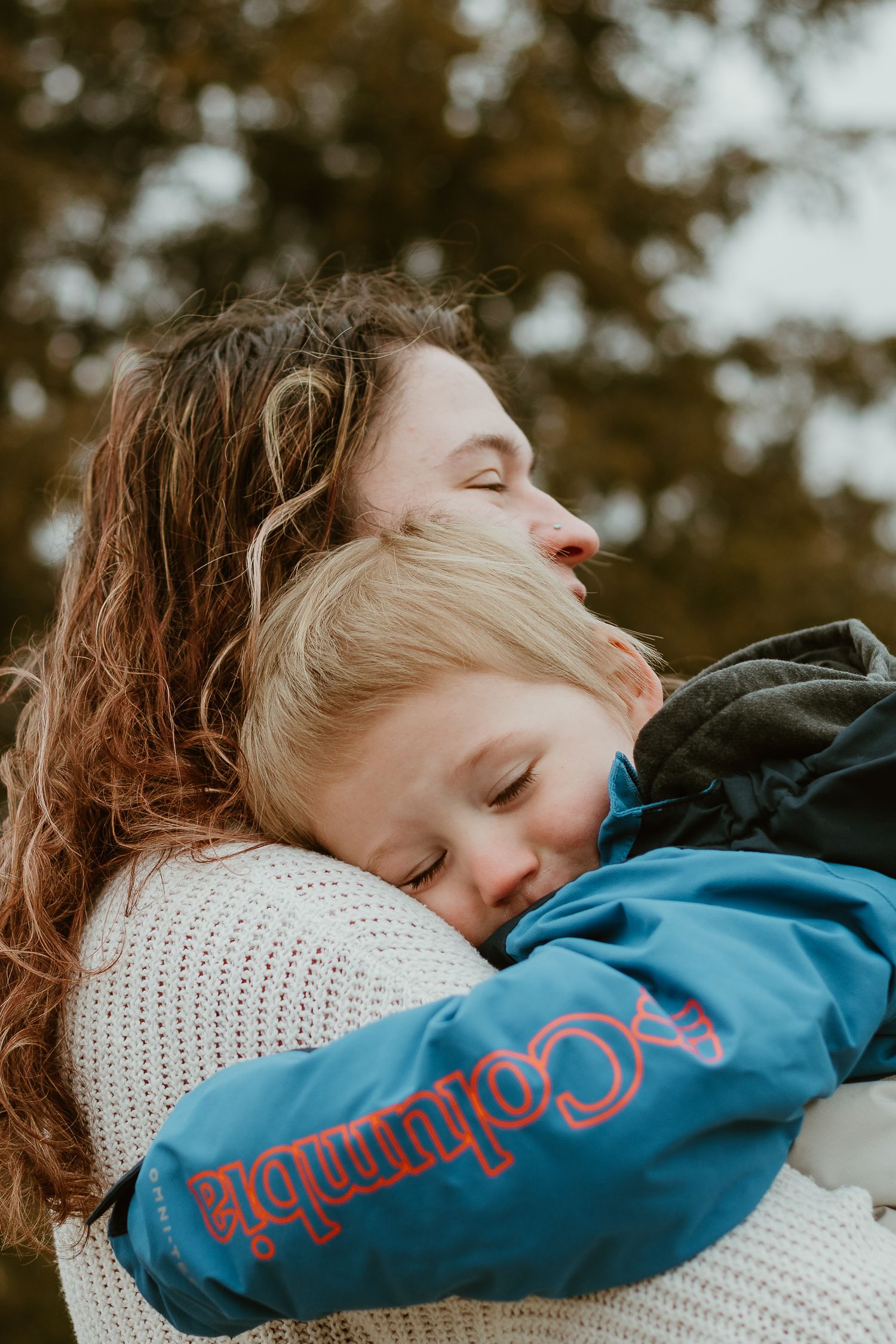 A tender moment captured in autumn shows a warm embrace between figures wearing a white sweater and blue Columbia jacket.