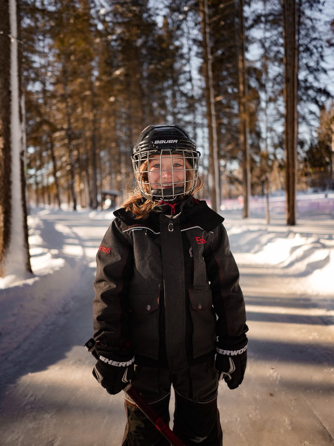 Winter sports enthusiast wearing protective hockey gear and dark jacket in snowy forest.