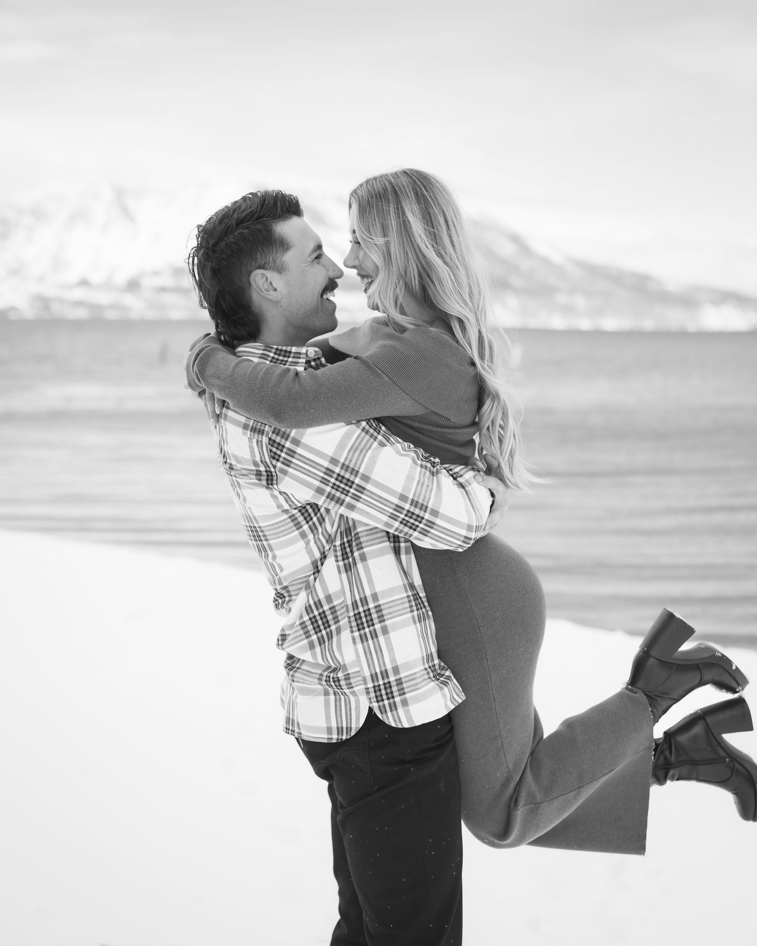 A romantic couple embraces in black and white photography with snowy mountains in the background.