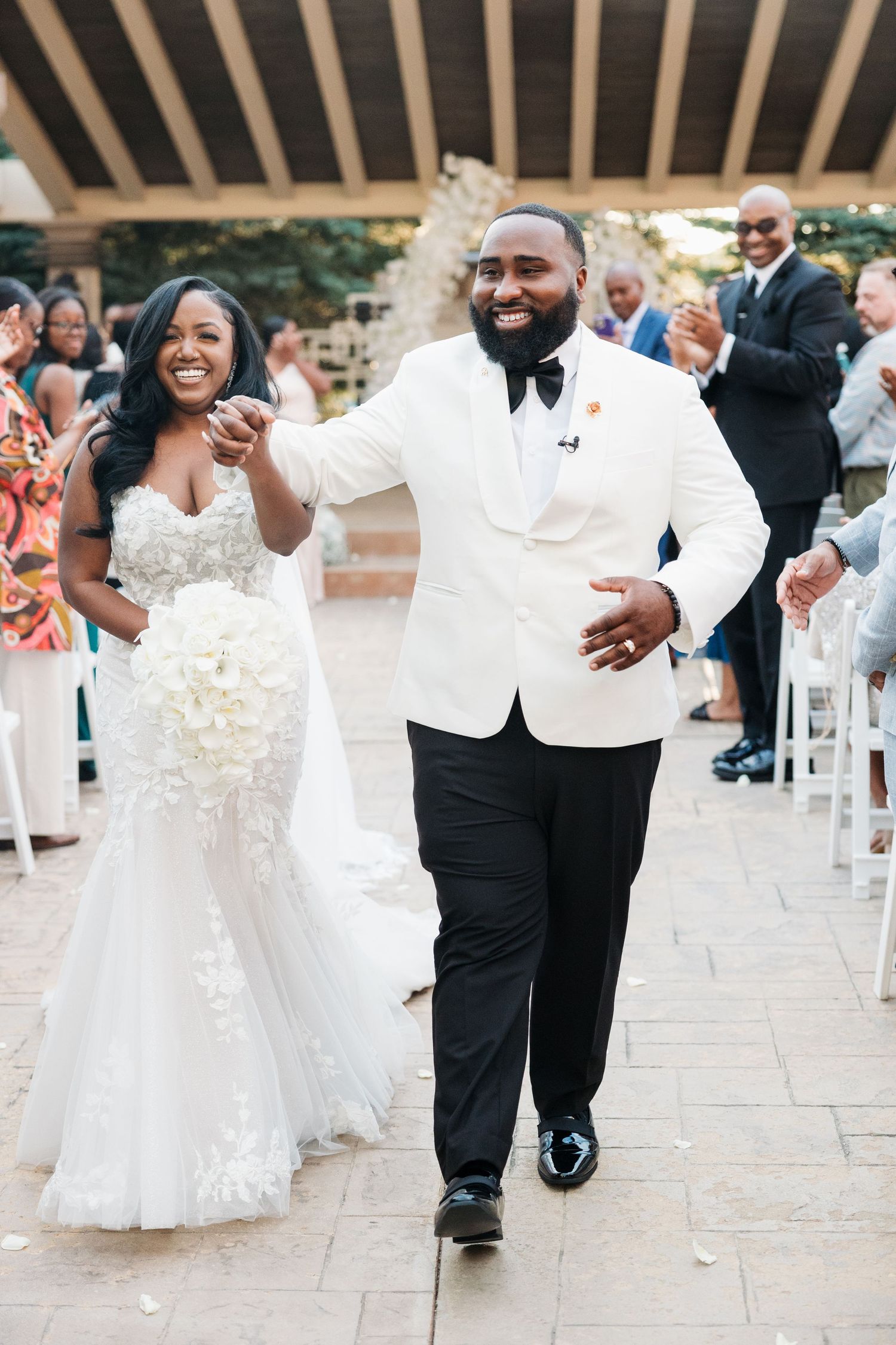 Joyful wedding celebration with dancing guests in formal attire on an outdoor stone patio.