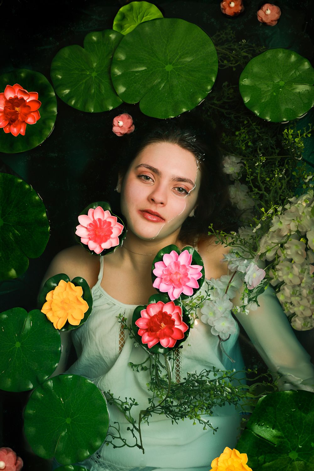 Girl in water surrounded by a dark green pond setting, looking directly at the camera
