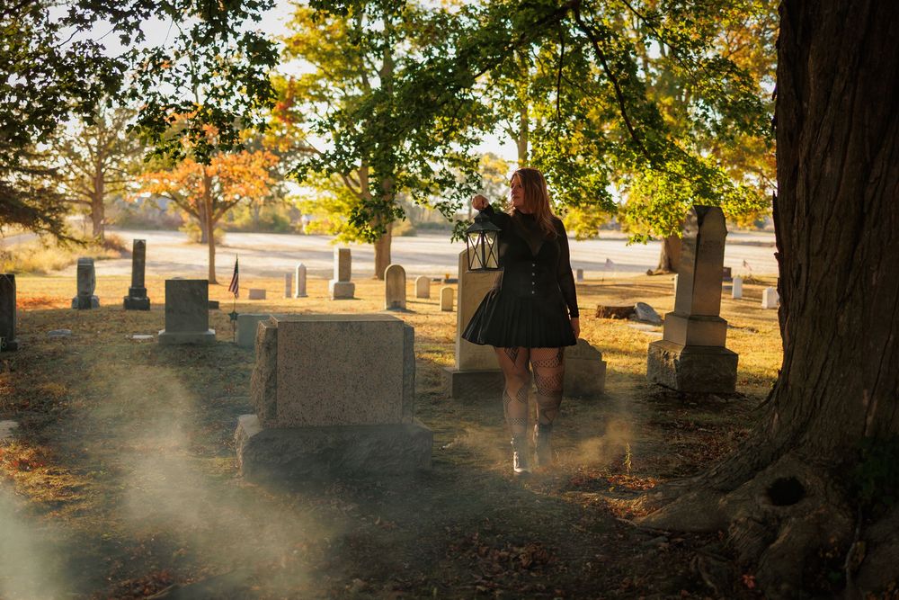 Sunlit autumn cemetery with gravestones casting long shadows among trees during golden hour.