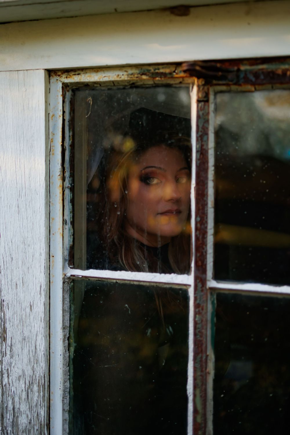 A mysterious figure peers through a series of old window panes in an eerie and atmospheric scene.