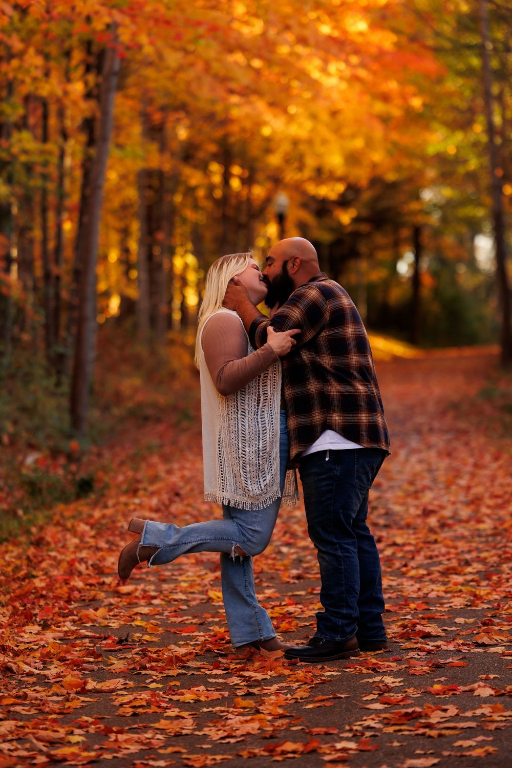 Two young children play together on a path covered in vibrant orange and red autumn leaves.