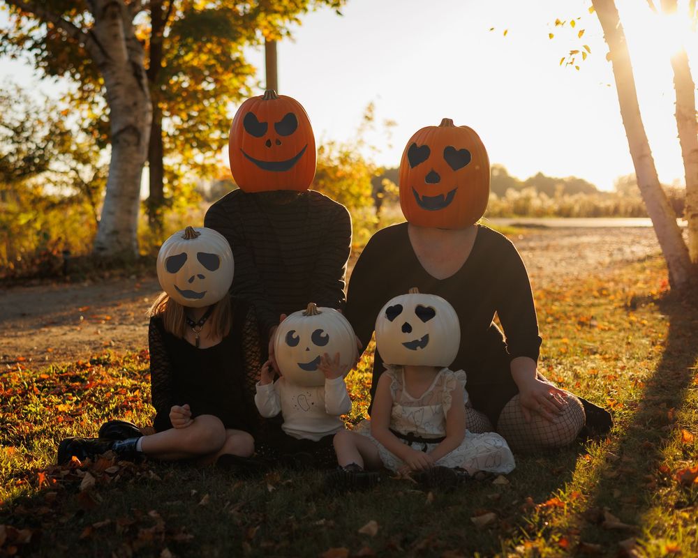 Halloween pumpkins and ghost plush toys arranged in autumn foliage during golden hour sunset.