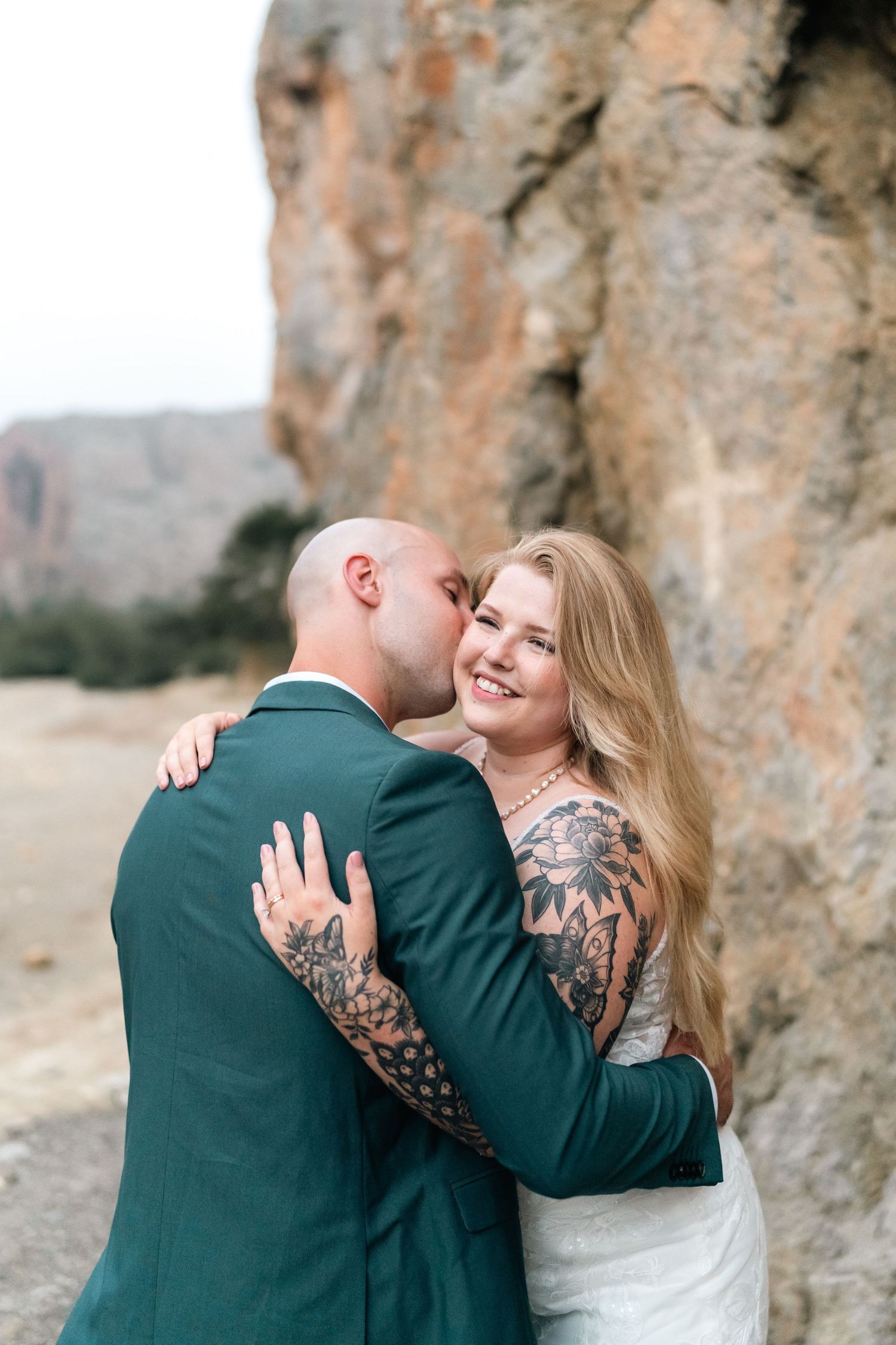 Couple in wedding attire sharing an intimate moment against rocky cliff backdrop.