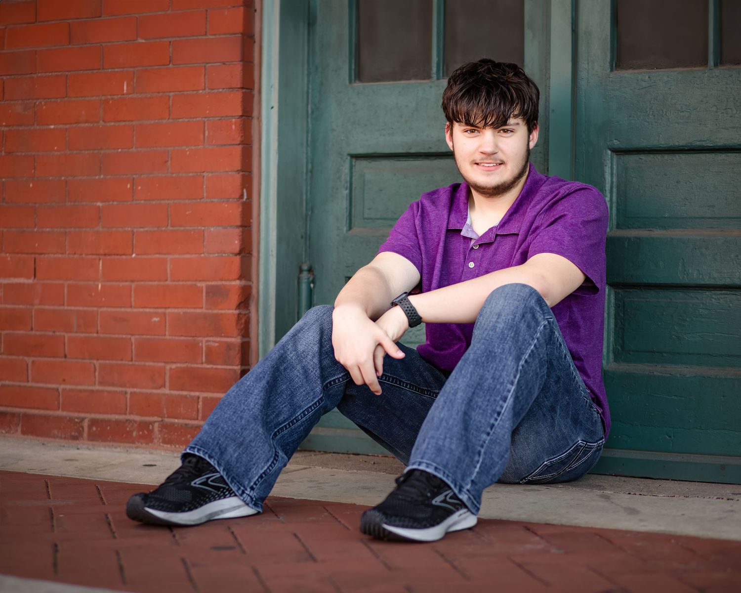 A casual portrait of someone in a purple shirt sitting on brick steps in front of a teal door.