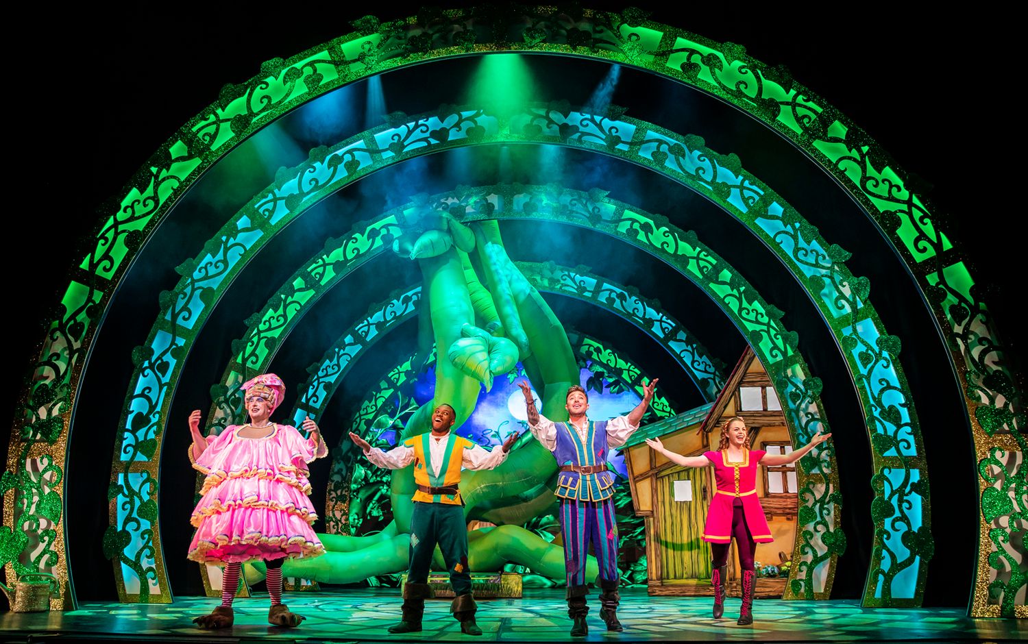 Theatrical stage with costumed performers under glowing green arches and vibrant lighting effects during a fantasy production.