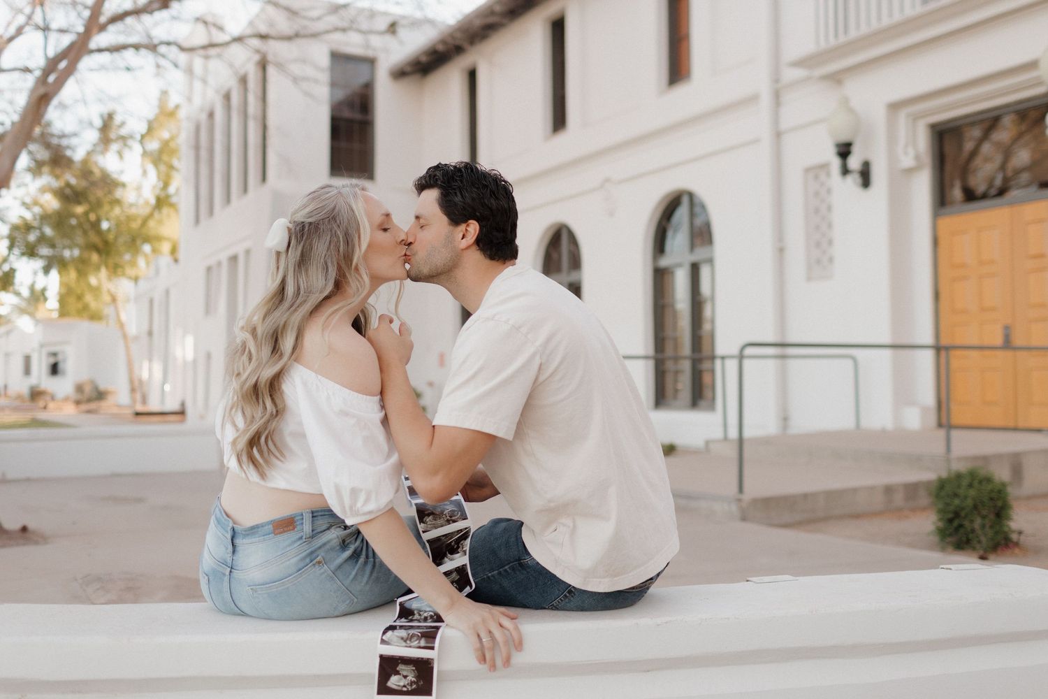 Intimate moment between couple sitting on concrete steps against white Mediterranean architecture.