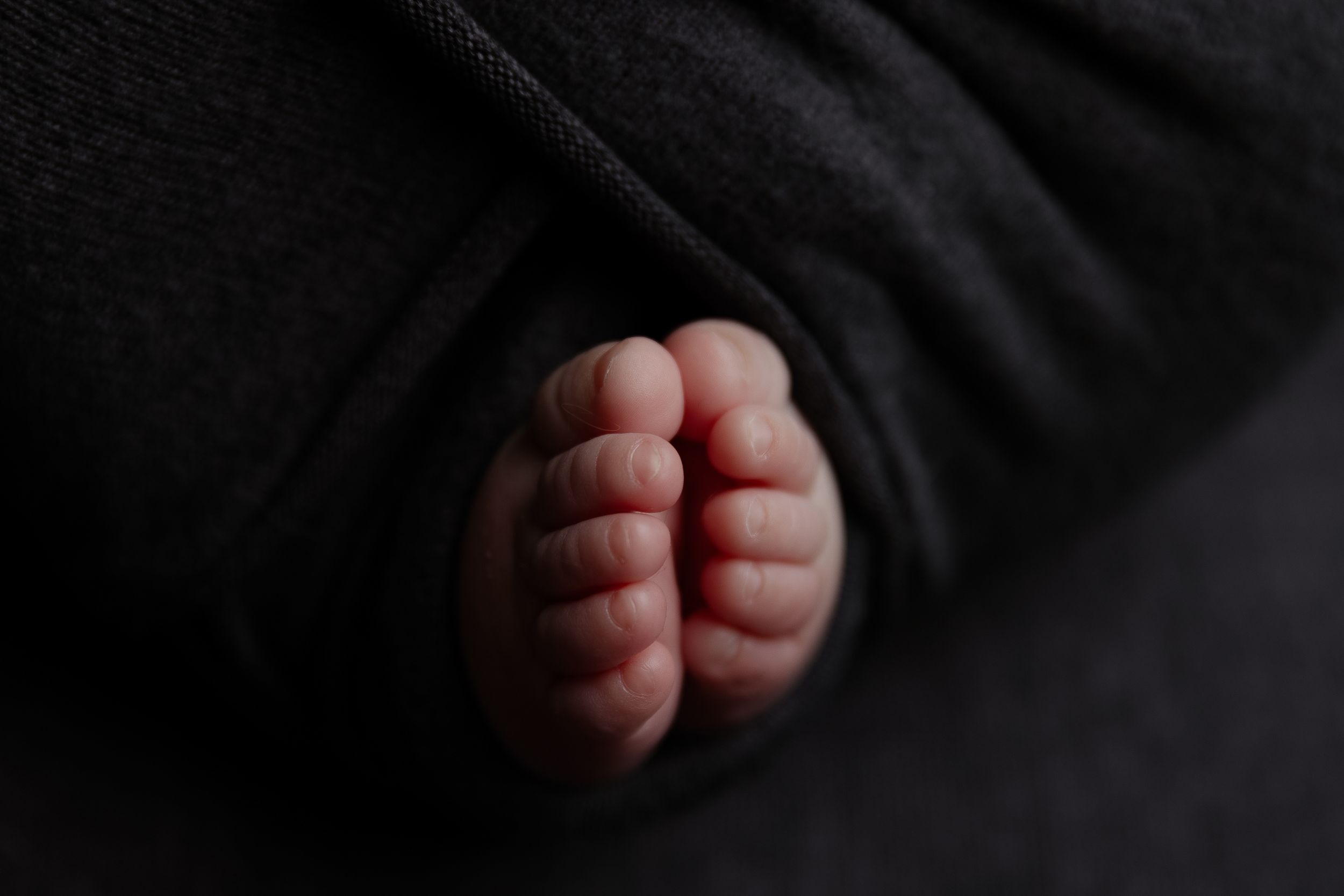 Close-up view of tiny baby feet against a dark background in moody lighting.