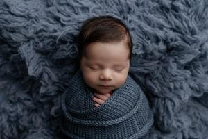 Sleeping newborn swaddled in cozy gray knit wrap on fluffy gray fur backdrop.