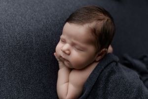 Peaceful sleeping newborn baby rests on dark gray blanket during professional photography session.
