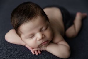 Peacefully sleeping infant resting on dark fabric during professional newborn photography session.