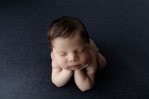 Peaceful sleeping newborn nestled on dark backdrop in froggy pose during professional photography session.