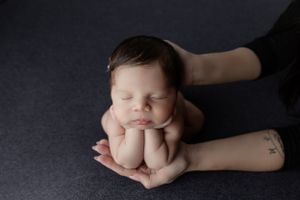 Gentle hands supporting sleeping newborn on dark fabric during intimate portrait session.